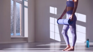 Woman with yoga mat with snow falling outside the window. Showing a commitment to stay motivated to exercise during winter